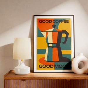 Peut inclure: Une affiche encadrée avec une illustration rétro d'une cafetière en orange, turquoise et jaune. Le texte "GOOD COFFEE GOOD MOOD" est affiché au-dessus et en dessous de la cafetière. Une lampe blanche, un vase blanc et un petit vase marron sont sur un meuble en bois.