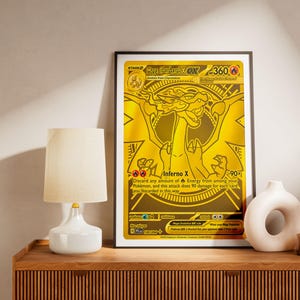 Puede incluir: Una impresión de tarjeta coleccionable enmarcada de color dorado que presenta al personaje Mega Charizard X. La tarjeta muestra el texto Mega Charizard X, 360 HP e Inferno X, con un dibujo lineal detallado sobre un fondo dorado metálico.