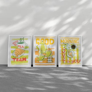 May include: Three framed art prints with breakfast-themed illustrations. The prints feature a cup of tea, a teapot, and a coffee cup, along with the words "TEA TEAM", "GOOD MORNING", and "JUST for YOU". The artwork is in yellow, green, and orange.