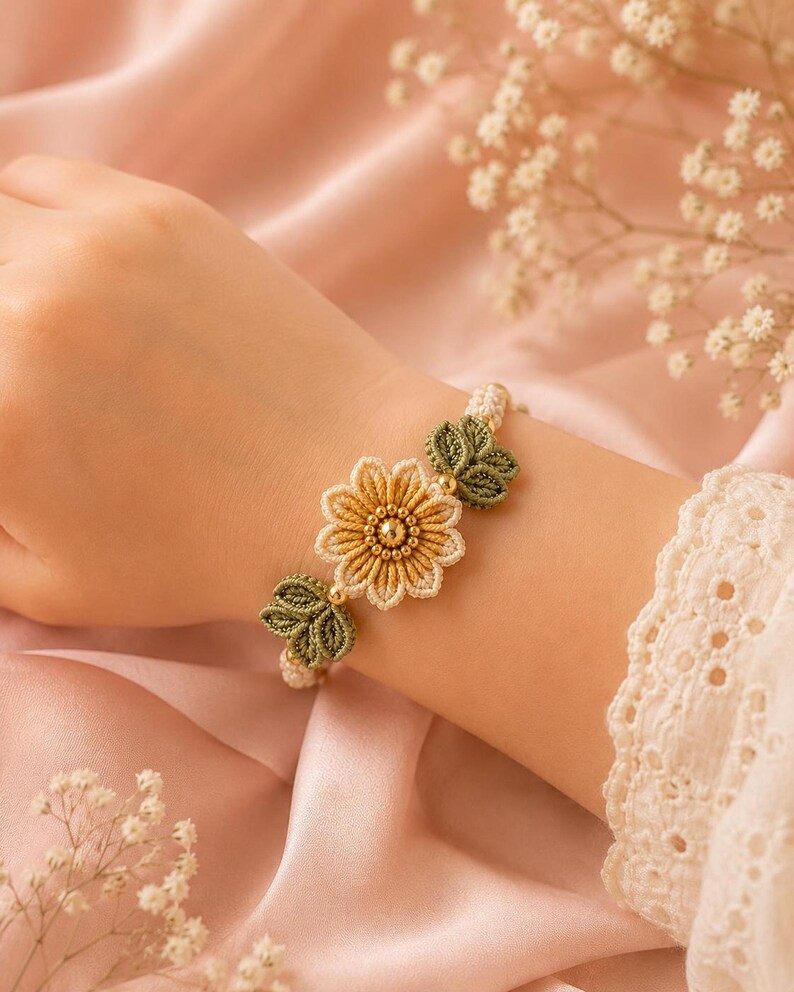 A hand wearing a beige and green crocheted bracelet with a central yellow flower and green leaves, on a pink satin fabric.