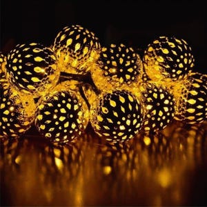 May include: A close-up of a string of decorative lights. Each light is a sphere with a black, patterned design, emitting a warm, golden light. The lights are clustered together, creating a warm, inviting glow against a dark backdrop.