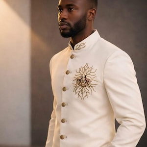 May include: Ivory-colored suit jacket with a mandarin collar and gold-colored buttons. The jacket features intricate gold embroidery on the chest and collar, creating a formal and elegant look.