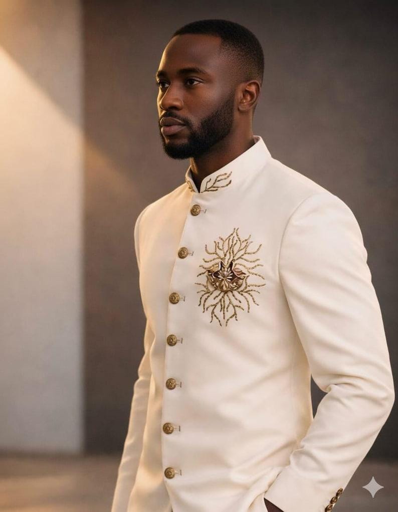 May include: Ivory-colored suit jacket with a mandarin collar and gold-colored buttons. The jacket features intricate gold embroidery on the chest and collar, creating a formal and elegant look.