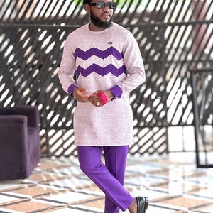 May include: A light purple long-sleeved shirt with a chevron design in dark purple, paired with matching purple pants. The outfit is completed with black loafers and sunglasses. The shirt has purple cuffs and a small logo.
