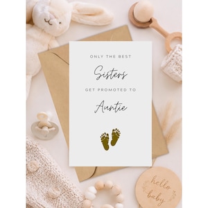May include: A white rectangular card with the black text ONLY THE BEST Sisters GET PROMOTED TO Auntie and two small gold baby footprints. The card is surrounded by a cream-colored plush rabbit, a wooden rattle, a pacifier, and a wooden disc.