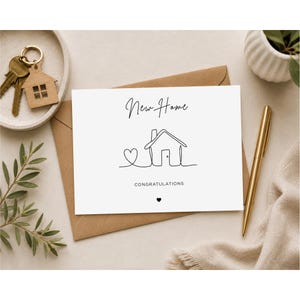 May include: A white greeting card with the words "New Home" and "Congratulations" in black script. The card features a line drawing of a house and heart. A gold pen, keys, and a small house-shaped keychain are also visible.