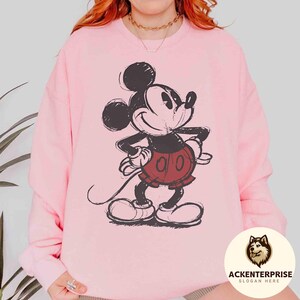 Puede incluir: Sudadera rosa claro con un dise&ntilde;o desgastado de Mickey Mouse. El personaje de dibujos animados est&aacute; representado en negro, rojo y blanco, sonriendo. La sudadera tiene cuello redondo y mangas largas.
