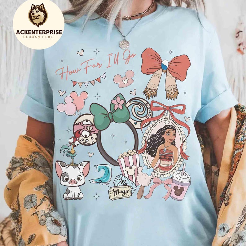 May include: Light blue t-shirt featuring a colorful graphic design with the text "How Far I'll Go". The design includes cartoon characters, bows, and other decorative elements. The shirt has rolled-up sleeves.