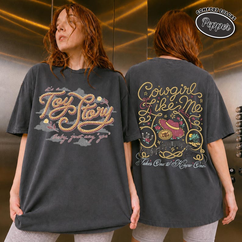 May include: A charcoal grey short-sleeve t-shirt featuring a front graphic with rope-style text reading Toy Story and baby, just say yes. The back graphic features rope-style text reading Cowgirl Like Me and Takes One to Know One.