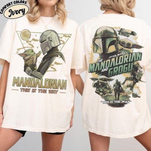 May include: Ivory-colored t-shirt featuring a graphic of The Mandalorian and Grogu. The front design includes the text "MANDALORIAN - THIS IS THE WAY". The back design features the text "STAR WARS THE MANDALORIAN AND GROGU" and "THIS IS THE WAY".
