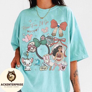 May include: A light blue t-shirt with the text "How Far I'll Go" and various cartoon graphics. The graphics include a portrait, a bow, a headband, and other cartoon elements. The shirt has a relaxed fit.