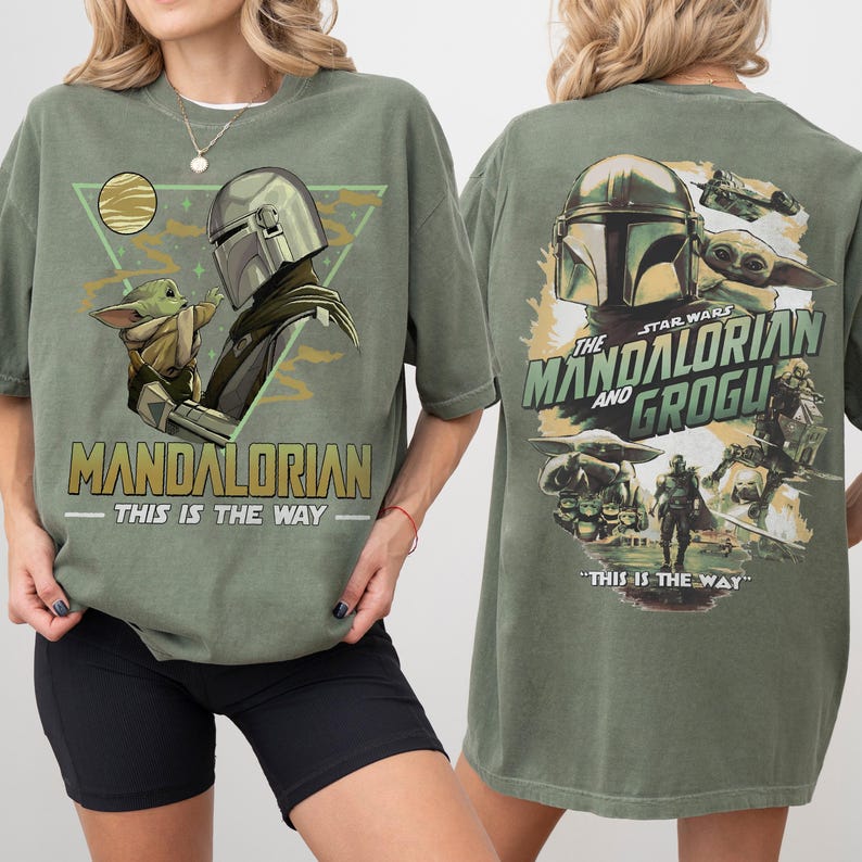 May include: Olive green t-shirt featuring a graphic of The Mandalorian and Grogu. The front design includes the text "MANDALORIAN" and "THIS IS THE WAY". The back of the shirt displays the Star Wars logo and the text "THE MANDALORIAN AND GROGU".