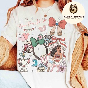 May include: Cream-colored t-shirt featuring a colorful graphic design with the text "How Far I'll Go." The design includes cartoon characters, bows, a portrait, and other decorative elements. The shirt has a round neckline and short sleeves.