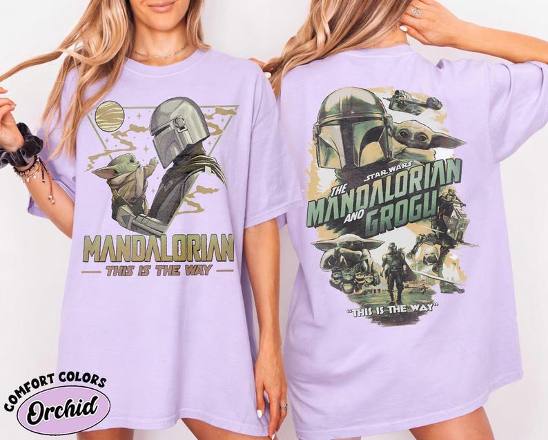 May include: A light purple t-shirt featuring a graphic of The Mandalorian and Grogu. The front design shows the Mandalorian and Grogu with the text "MANDALORIAN" and "THIS IS THE WAY". The back design features the text "THE MANDALORIAN AND GROGU".