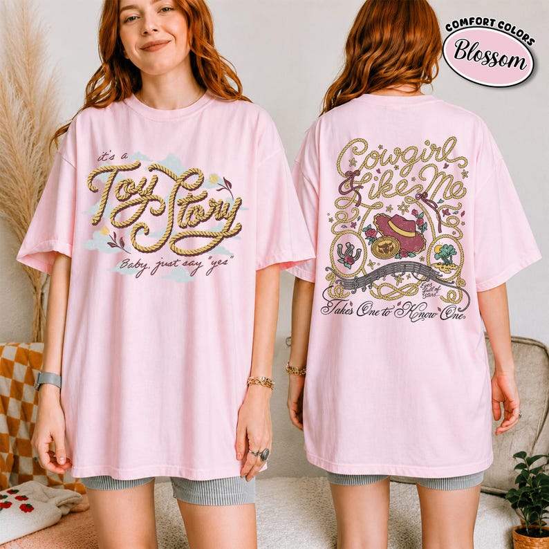 May include: A light pink short-sleeve t-shirt featuring a front graphic with rope-style text reading "it's a Toy Story Baby, just say "yes"" and a back graphic with rope borders, a hat, and text reading "Cowgirl like Me Takes One to Know One."