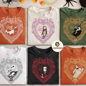 May include: Six folded t-shirts in various colors, each featuring a heart-shaped design with characters from "The Nightmare Before Christmas." The designs include Zero, Sally, Jack Skellington, and Oogie Boogie. The shirts are on a wooden surface.