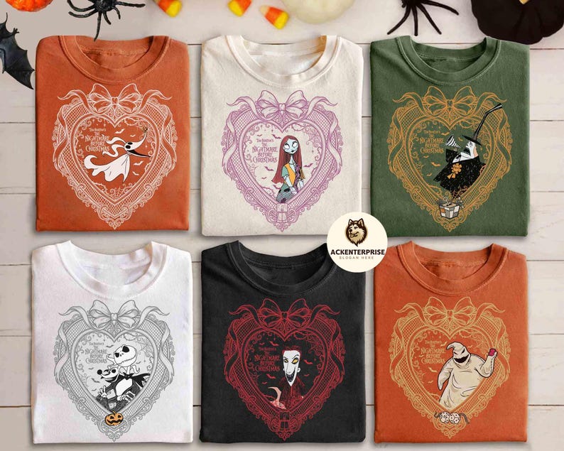 May include: Six folded t-shirts in various colors, each featuring a heart-shaped design with characters from "The Nightmare Before Christmas." The designs include Zero, Sally, Jack Skellington, and Oogie Boogie. The shirts are on a wooden surface.
