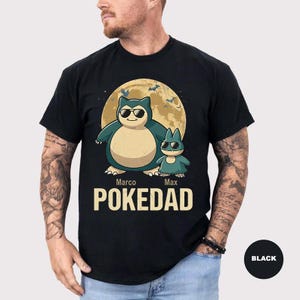 May include: A black short-sleeved t-shirt featuring a graphic of a large Snorlax and a smaller Munchlax wearing sunglasses in front of a full moon. The names Marco and Max are printed above the text POKEDAD in a bold, light-colored font.