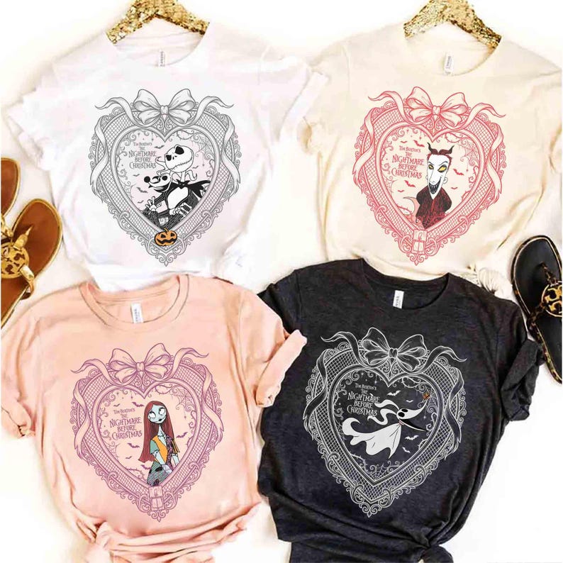 May include: Four t-shirts with different designs from The Nightmare Before Christmas. Each shirt features a heart-shaped design with characters like Jack Skellington and Sally. The shirts are white, cream, pink, and charcoal.