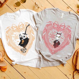 May include: Two t-shirts featuring characters from "The Nightmare Before Christmas." One is white with an orange heart design, and the other is gray with a pink heart design. Each heart contains a character illustration and the movie title.