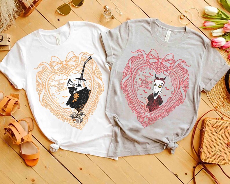 May include: Two t-shirts featuring characters from "The Nightmare Before Christmas." One is white with an orange heart design, and the other is gray with a pink heart design. Each heart contains a character illustration and the movie title.