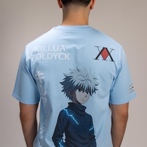 Op de afbeelding: Lichtblauw T-shirt met een afbeelding van een anime-personage met wit haar en blauwe ogen. De achterkant van het shirt toont de tekst "KILLUA ZOLDYCK" en Japanse tekst. Een rood en zwart dubbel X-symbool is ook aanwezig.