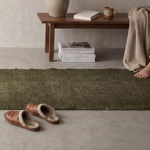 Peut inclure: Intérieur paisible avec un figuier lyre en pot, un tapis vert et des pantoufles en cuir marron. Un banc en bois accueille un vase avec des branches, un livre et une tasse. Une œuvre encadrée est accrochée au mur. Le tapis mesure environ 180 cm de long.