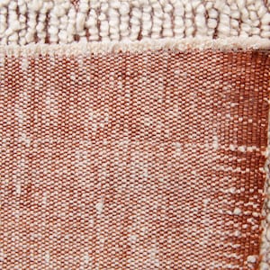 K&ouml;nnte beinhalten: Nahaufnahme eines strukturierten Teppichs in Braun- und Off-White-T&ouml;nen. Der Teppich hat ein gewebtes Design mit einem Fransenrand. Die Textur ist eine Kombination aus geschlungenen und flachen Webarten und erzeugt eine optisch ansprechende Oberfl&auml;che.