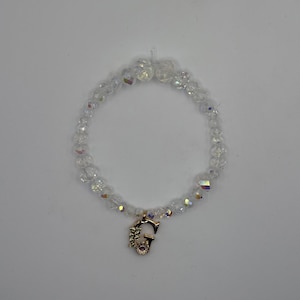 Op de afbeelding: Een heldere kralenarmband met een iriserende glans. De armband heeft een goudkleurige bedel in de vorm van de letter "G", versierd met bloemmotieven en een kleine paarse edelsteen. De kralen hebben een diameter van ongeveer 0,6 cm.