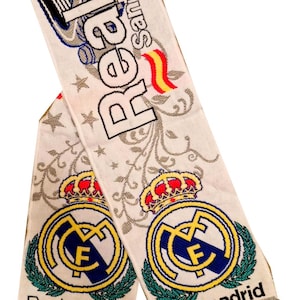 May include: White scarf with the Real Madrid logo, a gold crown, and the words "Real Madrid" in black. The scarf has a fringe at the bottom and the words "Real Santiago" at the top.