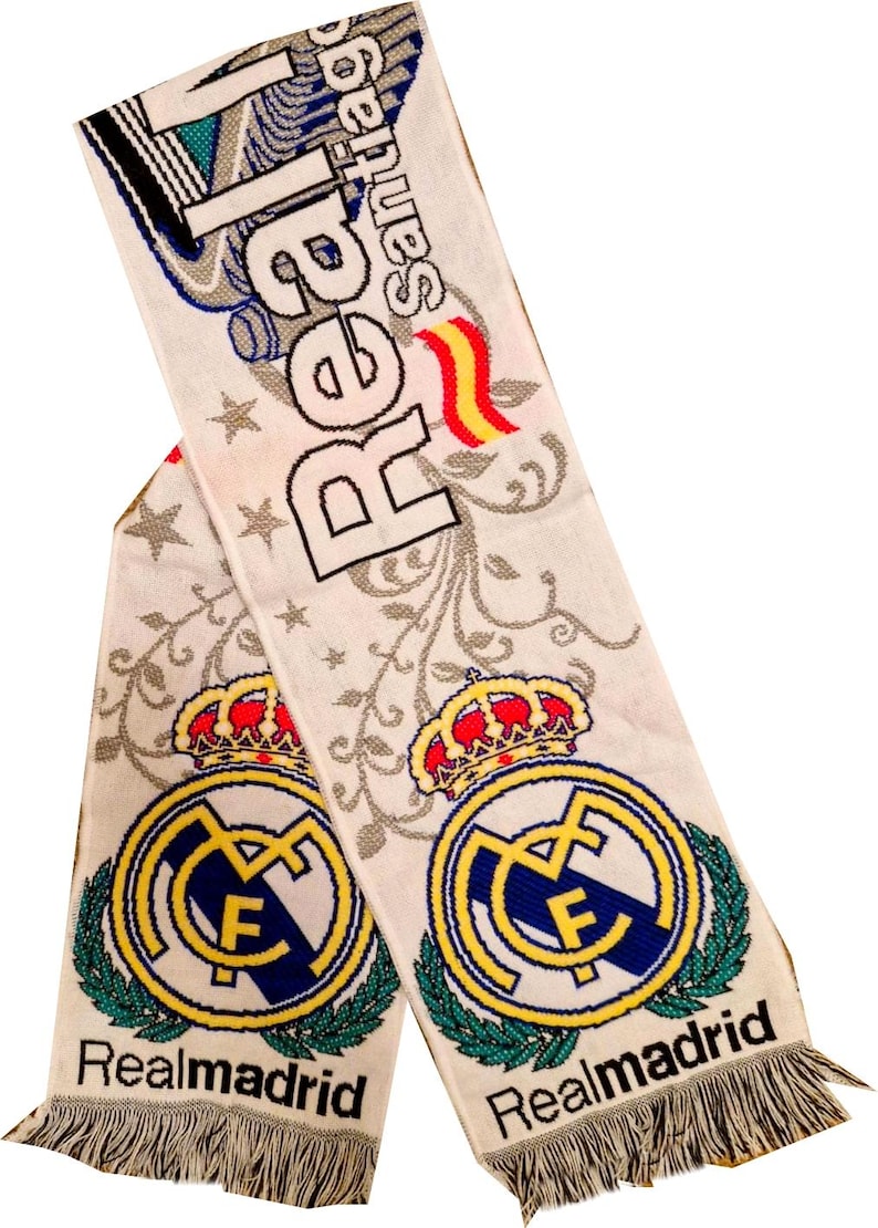May include: White scarf with the Real Madrid logo, a gold crown, and the words "Real Madrid" in black. The scarf has a fringe at the bottom and the words "Real Santiago" at the top.