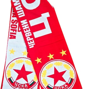 Puede incluir: Bufanda de punto roja y blanca con el texto "ЦСКА СОФИЯ" y "ЧЕРВЕНИ ШАМПИОНИ". La bufanda presenta un logotipo de estrella y estrellas amarillas. El borde inferior tiene flecos.