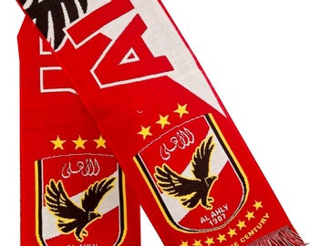 May include: A red and white scarf with the word "AL" in large white letters. The scarf features the team logo, a black eagle, and the text "AL AHLY 1907 CLUB OF THE CENTURY". The scarf has a fringed edge.