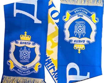 May include: A blue and white scarf with yellow accents and fringe. The scarf features a crest with the text "AHEПP" and "1960 MOGILEV". The design includes a crown, a shield, and a soccer ball.