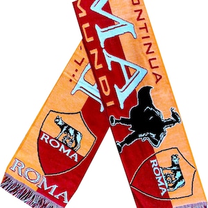 Peut inclure: Une écharpe en tricot rouge et orange avec le texte "CONTINUA LA MUNDI" en bleu clair, ainsi que deux écussons affichant le mot "ROMA" et un graphique de loup. L'écharpe comprend une silhouette noire d'une figure et des extrémités à franges.
