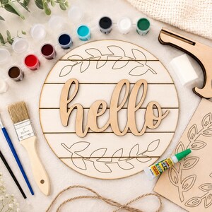 May include: A craft kit with a wooden sign that says "hello", surrounded by a leaf design. It includes paint pots in various colours, paintbrushes, glue, and a wooden stand. Ideal for home decoration projects.