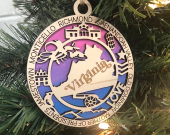 May include: A wooden Christmas ornament shaped like the state of Virginia with a colorful gradient design. The ornament features various landmarks and text including "Richmond", "Shenandoah Valley", "Jamestown", "Mother of Presidents", "Love", and "Old Dominion".