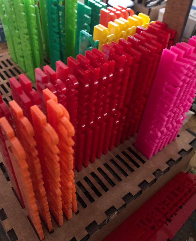May include: A collection of colorful, interlocking plastic pieces in shades of orange, red, yellow, green, and pink. The pieces are arranged in rows within a wooden tray, suggesting a building or design project. The pieces have a textured surface.