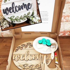 May include: A DIY craft kit for making a wooden welcome sign. The kit includes a pre-cut wooden sign, paint, a paintbrush, and glue. The sign features a welcome message with a leafy design.
