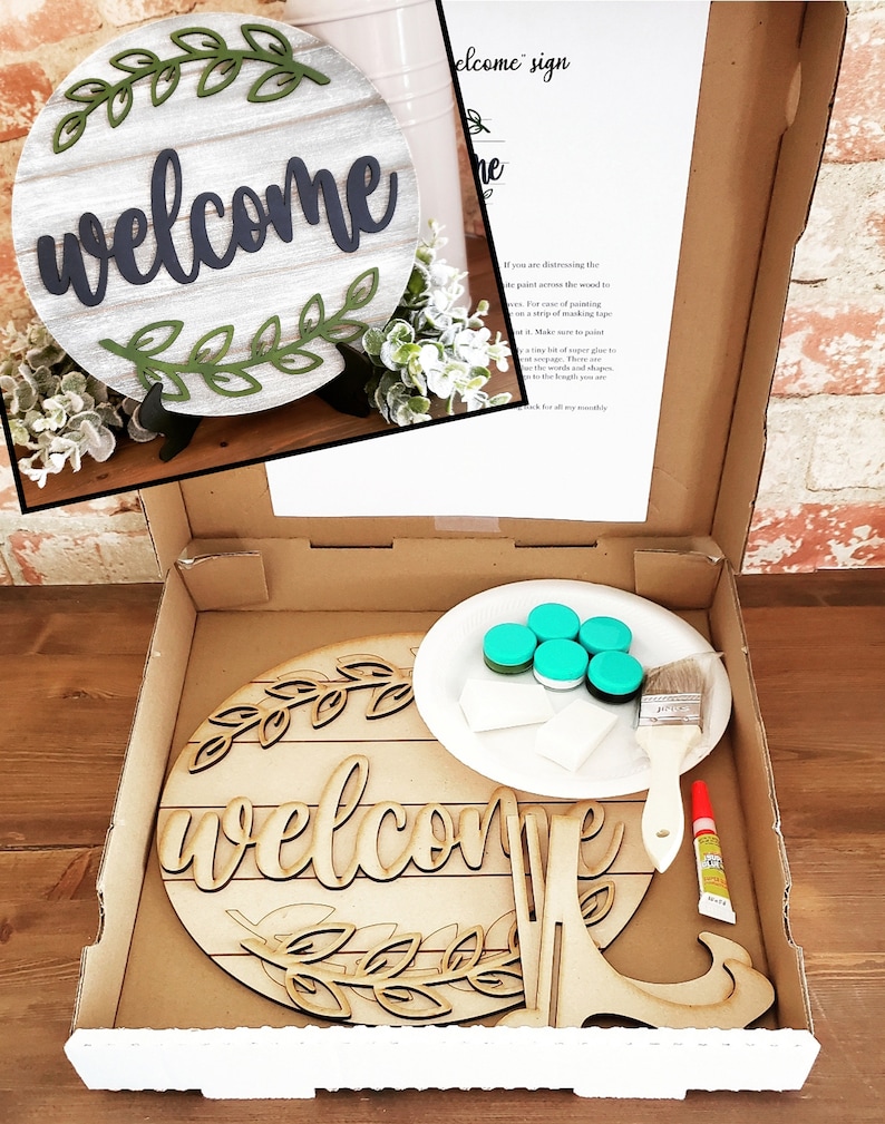 May include: A DIY craft kit for making a wooden welcome sign. The kit includes a pre-cut wooden sign, paint, a paintbrush, and glue. The sign features a welcome message with a leafy design.