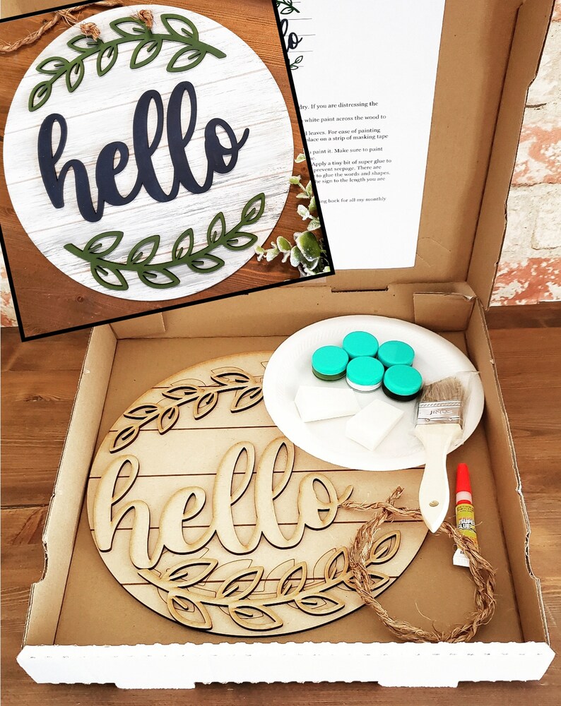 May include: A DIY craft kit for making a wooden "hello" sign. The kit includes a round wooden sign with the word "hello" cut out, a small plate of turquoise paint, a paintbrush, a roll of twine, and a tube of glue.