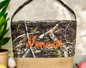 May include: Camouflage fabric Easter basket with a burlap bottom. The basket is personalized with the name "Bennett" in orange thread.