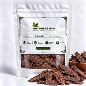Puede incluir: Una bolsa blanca vertical etiquetada como The Spices Hub que contiene vainas de Shikakai secas. La etiqueta presenta iconos de hojas verdes y texto que incluye 100% Natural, No Additives, Premium Quality y Aromatic. Una ventana muestra las vainas.