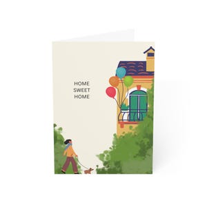May include: Greeting card with a whimsical illustration. The card features a house with a balcony and colorful balloons. A person walks a dog on a leash in front of the house. The words "HOME SWEET HOME" are printed on the card.