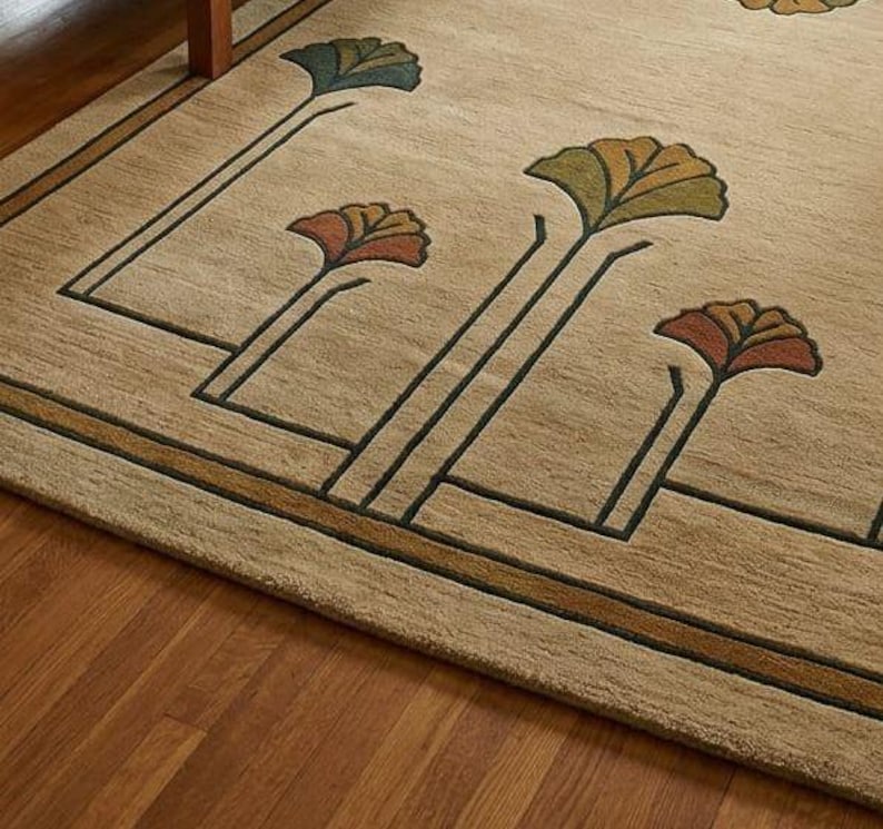 May include: A beige area rug featuring a dark brown linear border and stylized fan-shaped floral motifs in shades of teal, olive green, and burnt orange. The rug has a textured pile surface with clean geometric lines and symmetrical plant patterns.