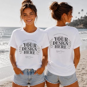 Könnte beinhalten: Zwei weiße T-Shirts mit dem Text "YOUR DESIGN HERE" werden gezeigt. Die Shirts werden mit Jeansshorts an einem Strand getragen. Der Text ist von einem Lorbeerkranz umgeben. Die Worte "MOCKUPS THAT STAND OUT" und "Styled Scene" sind ebenfalls aufgedruckt.
