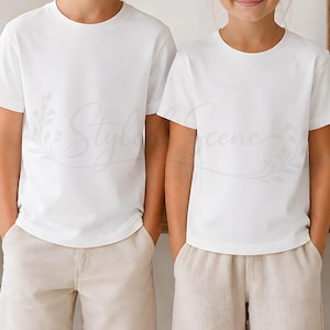 Puede incluir: Dos ni&ntilde;os con camisetas blancas de cuello redondo y pantalones cortos beige. Las camisetas son lisas y de manga corta. Los ni&ntilde;os est&aacute;n uno al lado del otro, con las manos en los bolsillos.