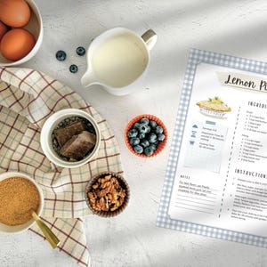 Peut inclure: Vue a&eacute;rienne des ingr&eacute;dients pour une recette de tarte au citron. Comprend des &oelig;ufs, de la farine, du sucre, des myrtilles, du chocolat, des noix et une cruche de lait. Une fiche de recette avec le titre "Lemon Pie" est &eacute;galement visible.