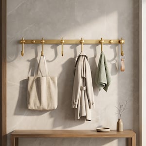 Peut inclure: Un porte-manteau en métal doré avec sept crochets, tenant un sac fourre-tout beige, un manteau clair, une serviette verte et un porte-clés. Le porte-manteau est fixé sur un mur carrelé gris clair au-dessus d'un banc en bois.