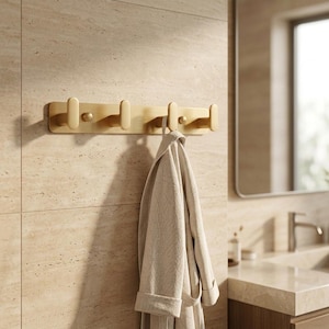 May include: A wooden wall-mounted coat rack with four hooks. The rack is a light wood color and has a simple, modern design. A light gray robe hangs from one of the hooks. The background is a bathroom setting.